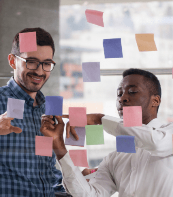 Two men looking at sticky notes on glass talking